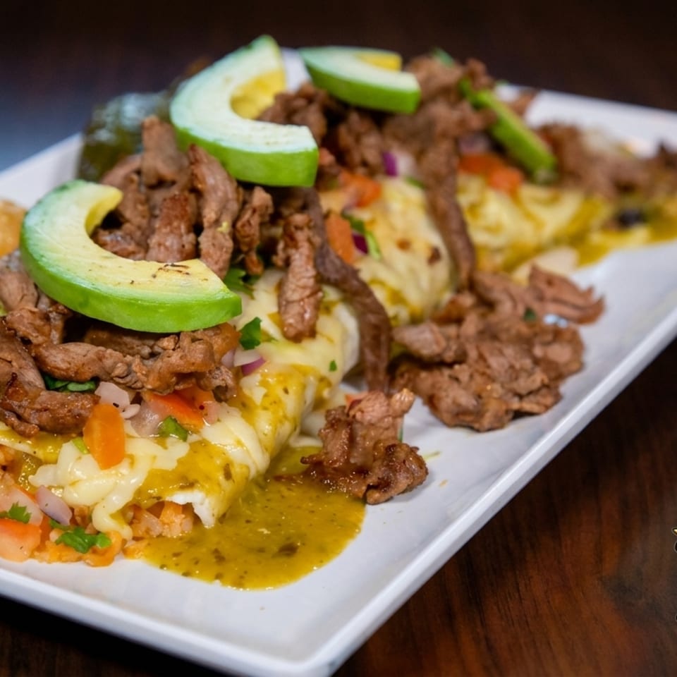 Santa Lucia Mexican Restaurant's enchiladas topped with steak, avocado, and green sauce on a white plate.