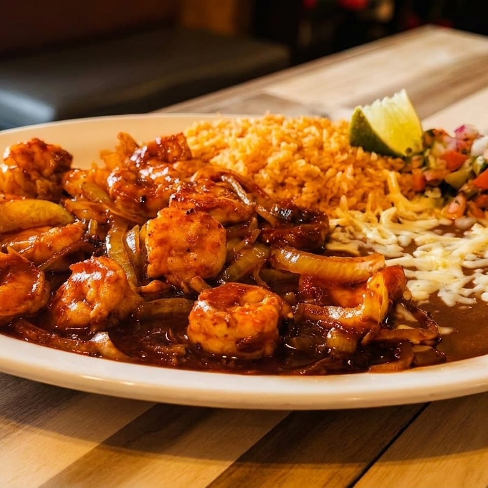 Shrimp with onions in a rich sauce, served with rice, refried beans, pico de gallo, and a lime wedge.